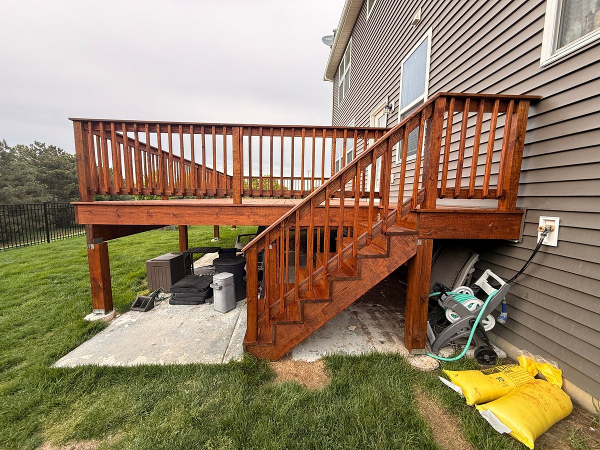Wooden deck attached to house with stairs, storage items and yard equipment underneath
